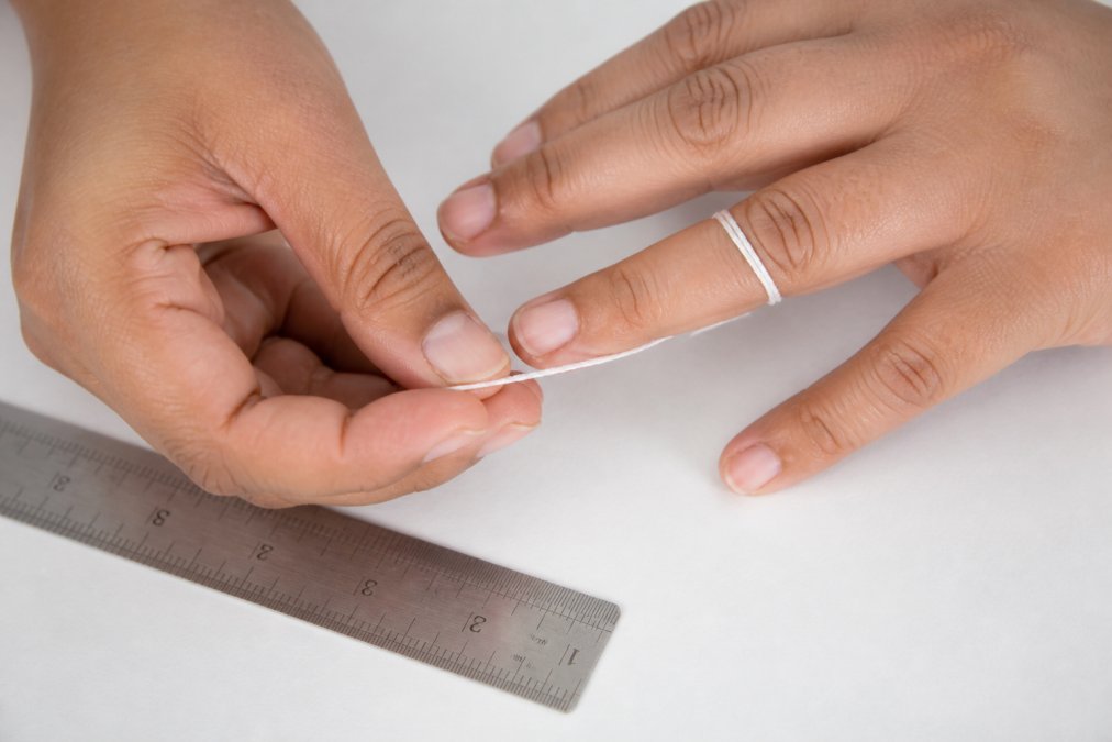 Hands wrapping a piece of string around a finger next to a ruler to measure ring size for a printable chart