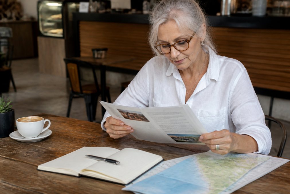 A traveller reviewing a printed itinerary and map at a café table with a notebook and pen, planning their journey