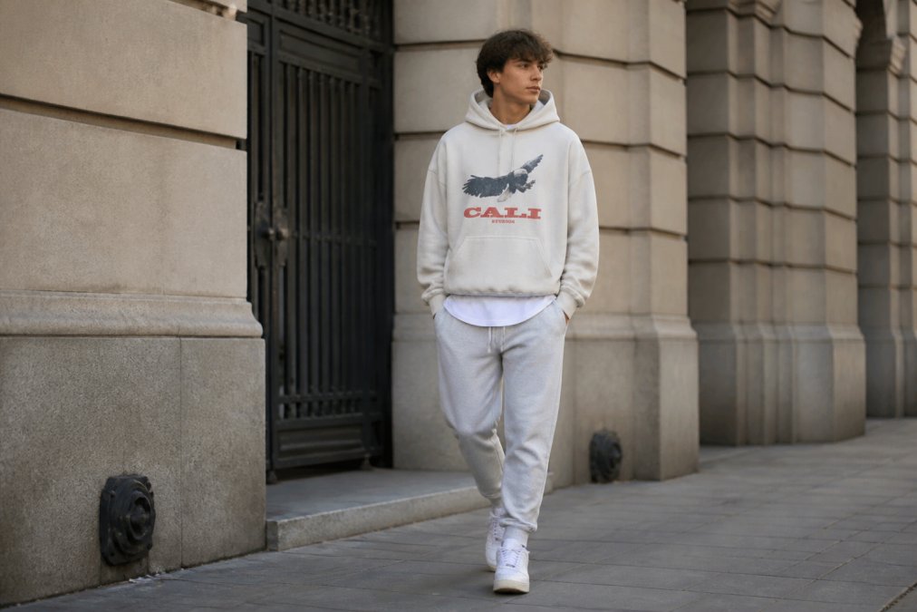Street style shot of a man wearing an oversized hoodie layered with a fitted t-shirt underneath and tapered joggers, demonstrating balanced proportions in urban setting with natural daylight