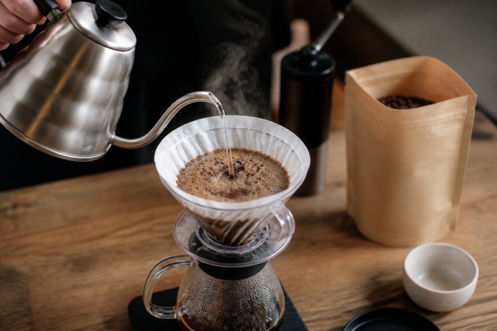 Hot water blooming over ground beans to reveal the freshest coffee in a pour-over dripper on a wooden counter.