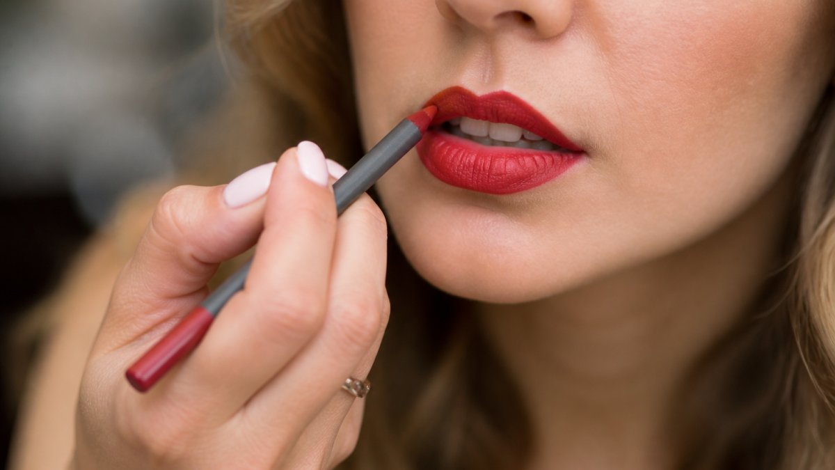 Close-up of hands applying red lipstick with precision lip liner, showing proper technique and control on lips