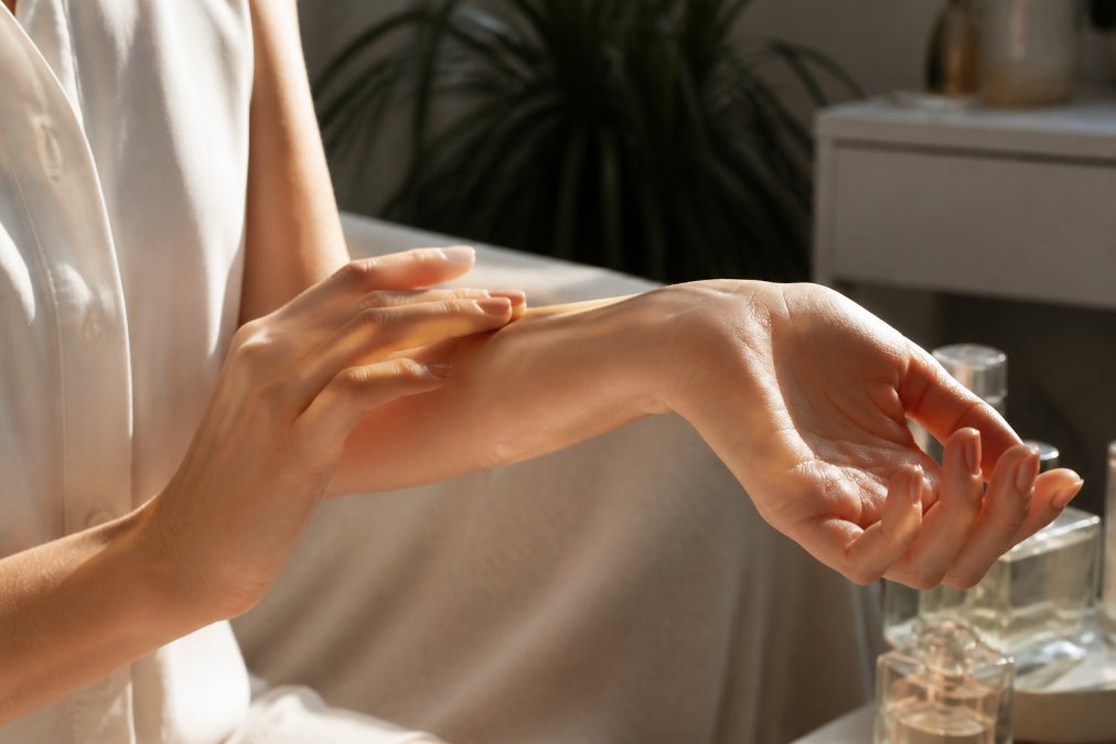 Close-up of a person's wrist showing perfume application to inner arm, with natural sunlight illuminating the skin and a second hand positioned to demonstrate proper testing placement on pulse point