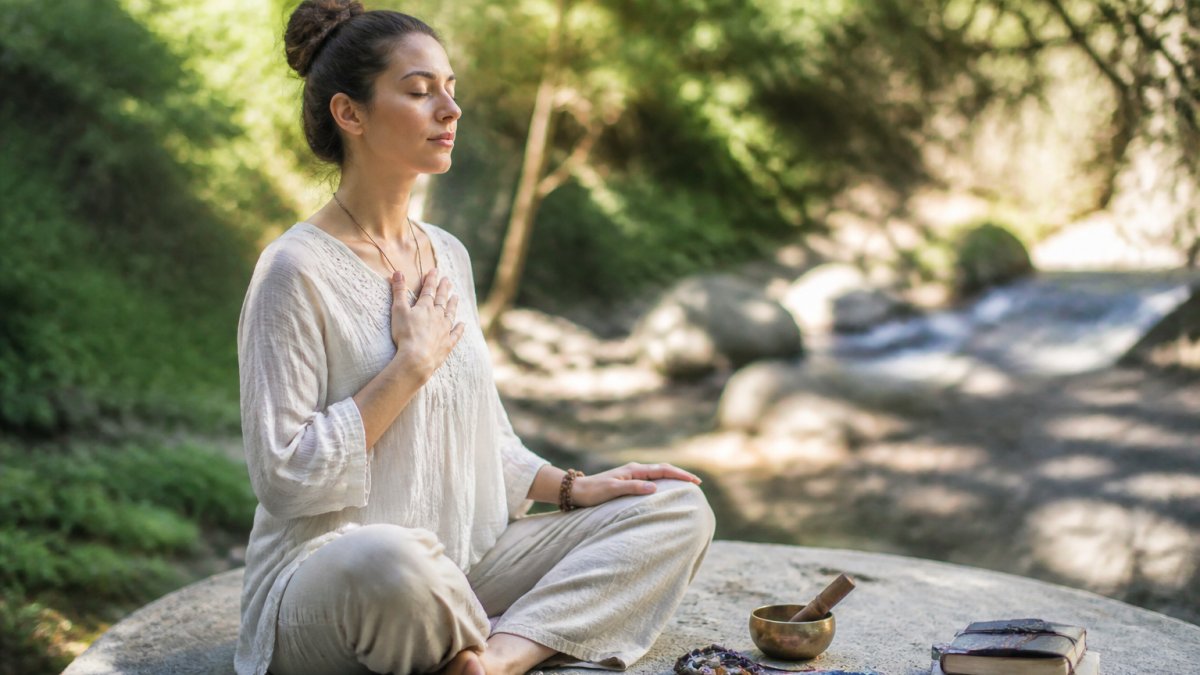 How to Find Your Spiritual Purpose in Life 1 Woman sitting peacefully in nature with a hand on her heart in quiet reflection