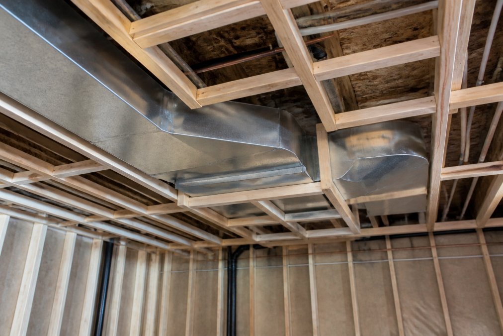 Basement ceiling showing HVAC ductwork with wooden furring frame built around it, demonstrating clearance and framing technique