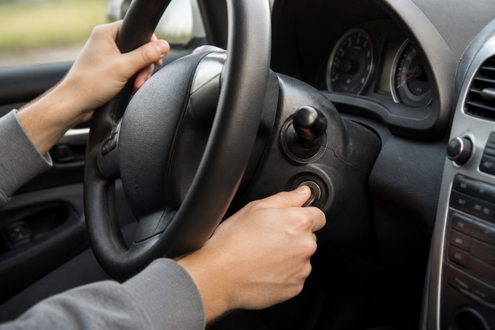 Close-up of driver's hands gripping the steering wheel while attempting to turn a car key in the ignition, showing the gentle jiggling motion with natural dashboard lighting