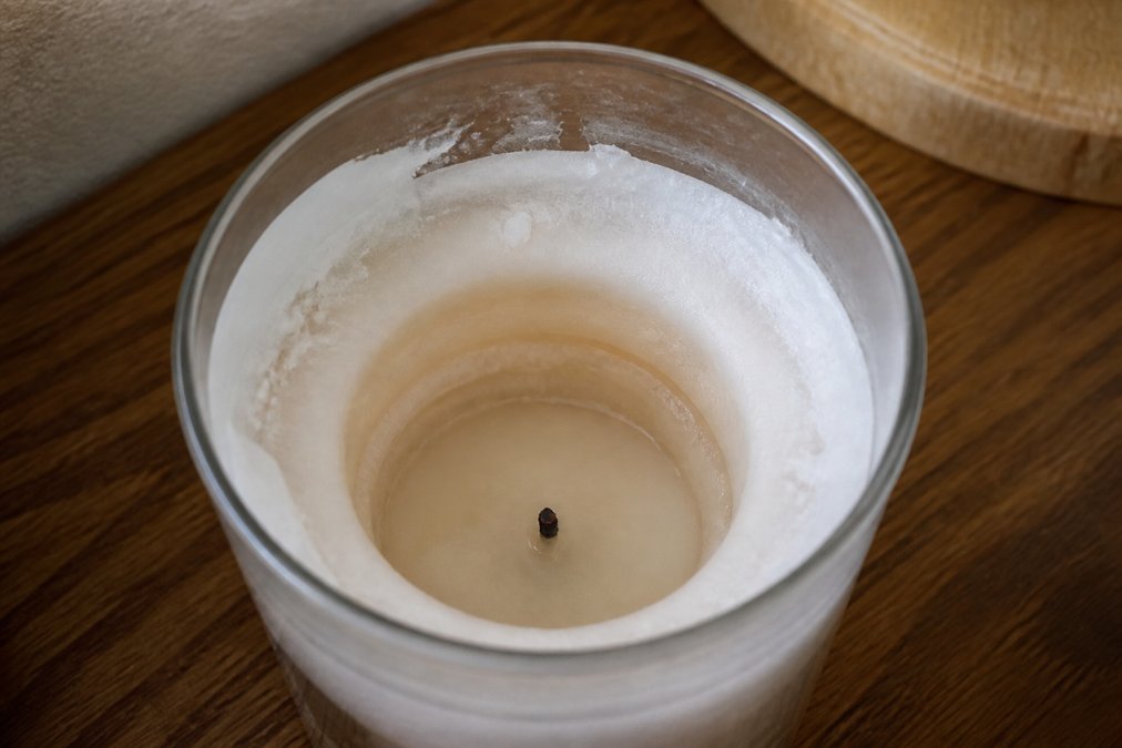 Close-up of a tunneled candle jar showing exposed wick in center with unmelted wax buildup along the sides and walls of the glass container