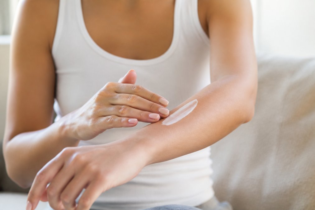 Close-up of hands gently applying a white cream moisturizer to a forearm, showing the application technique on clean, dry skin in soft natural light