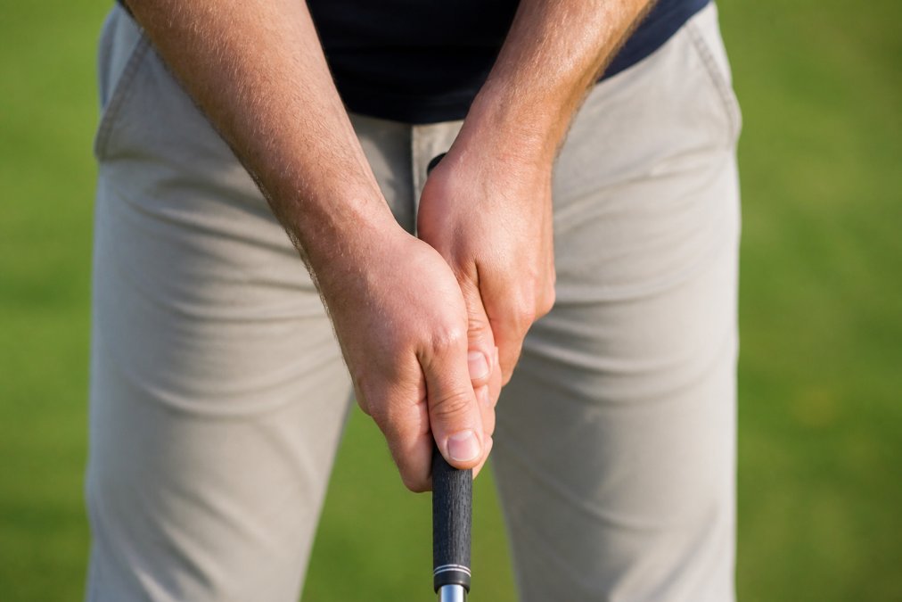 Close-up of golfer's hands gripping a golf club, showing the V-shape alignment between thumb and forefinger pointing toward the right shoulder, with proper finger positioning on the grip