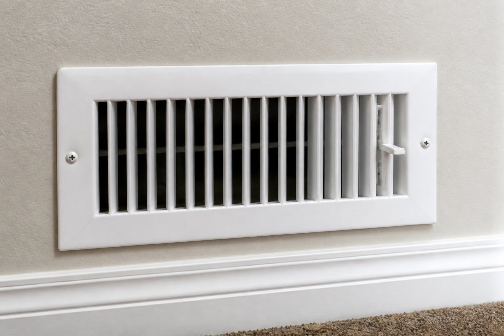 Close-up of a supply register on an interior wall with the damper lever visible in the fully open position, showing proper airflow orientation