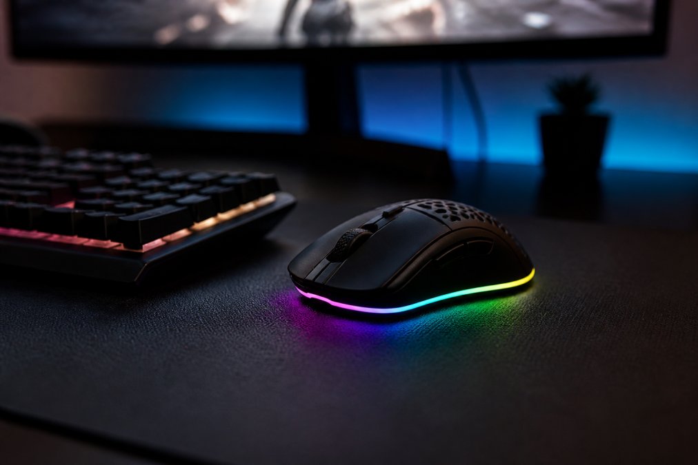 Sleek black gaming mouse with RGB lighting on a desk mat next to a mechanical keyboard in a dimly lit room
