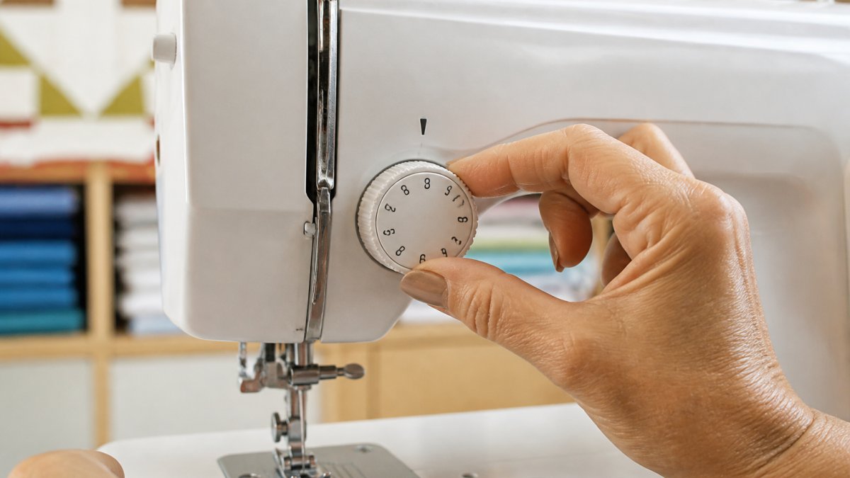 Close-up of hands adjusting the sewing machine tension dial with the presser foot raised to begin calibration.