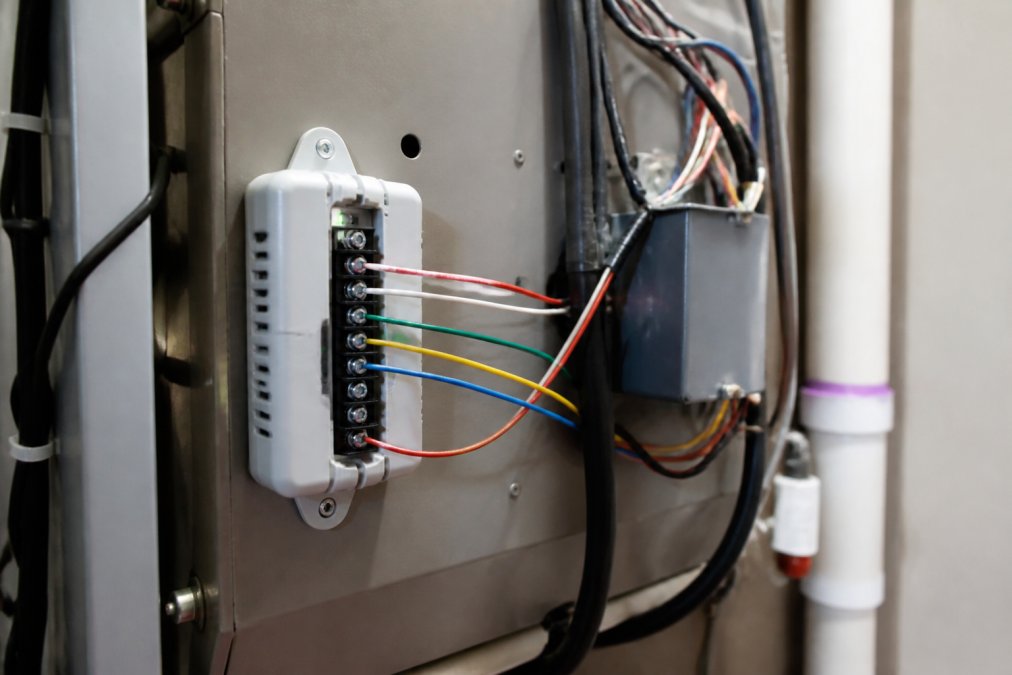 Power extender kit mounted on furnace cabinet with color-coded wires connected to terminal blocks, showing proper wire routing and labeling in clear workshop lighting