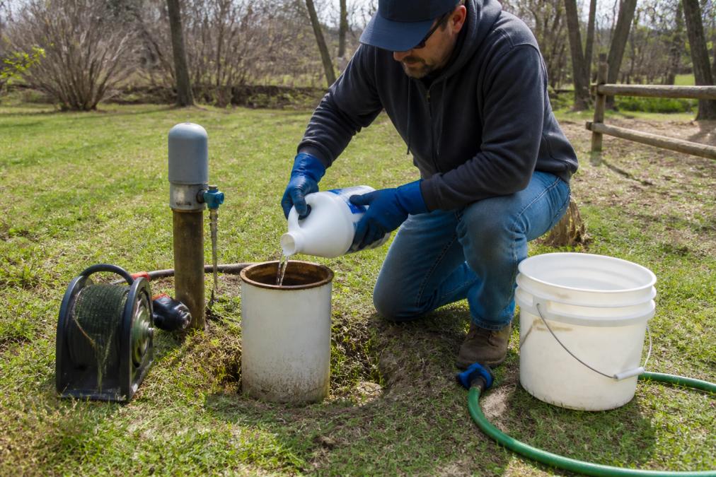 Homeowner wearing gloves pouring bleach into a well casing to treat well water sulfur smell