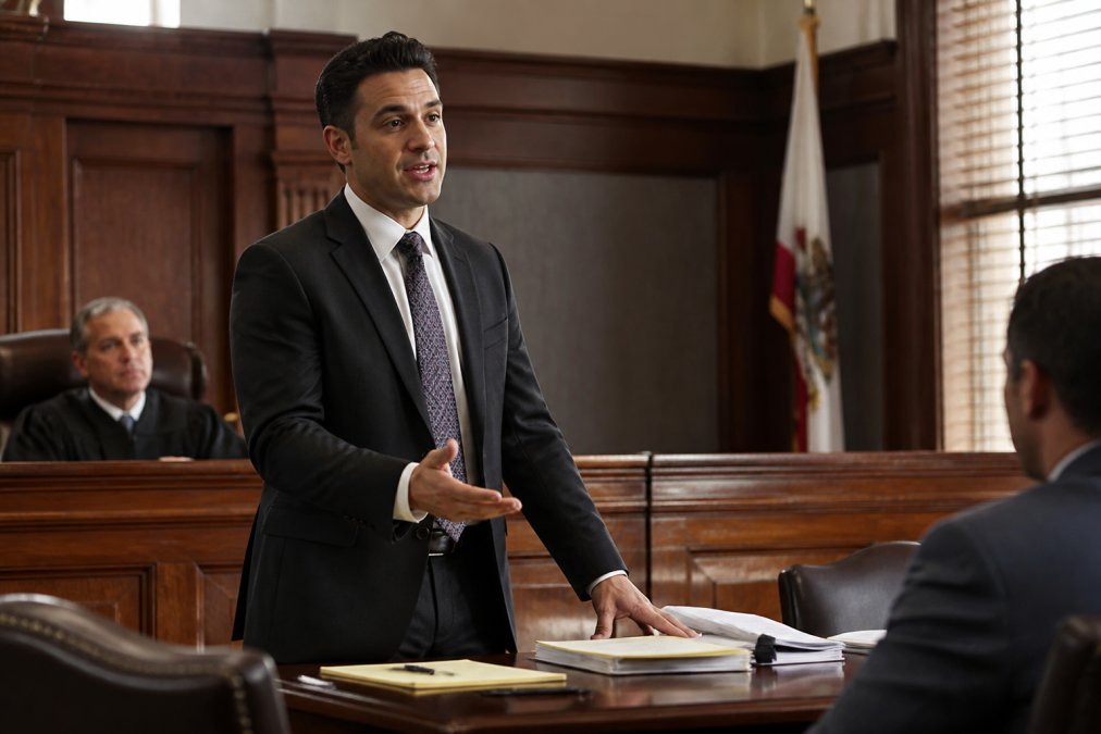 Lawyer standing in a courtroom with confidence, speaking with legal documents and a notepad visible on the desk with natural courtroom lighting