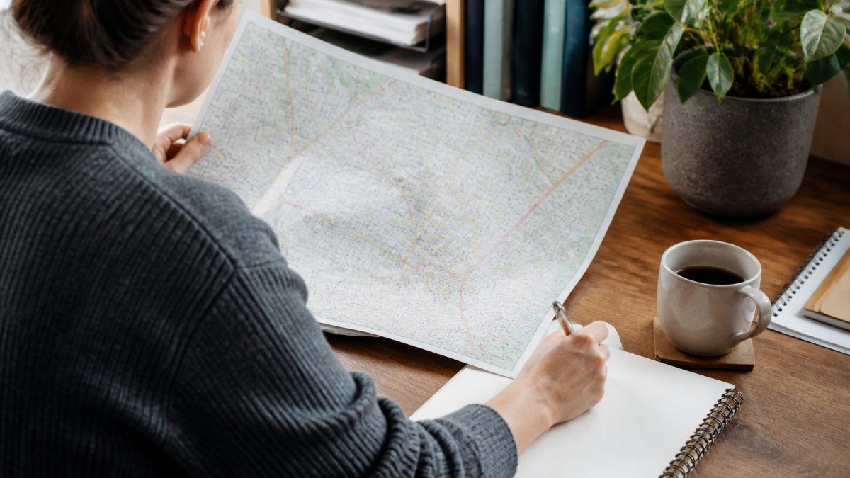 Person sitting at desk with laptop, viewing a postcode crime map on screen, with notepad and pen nearby for recording information