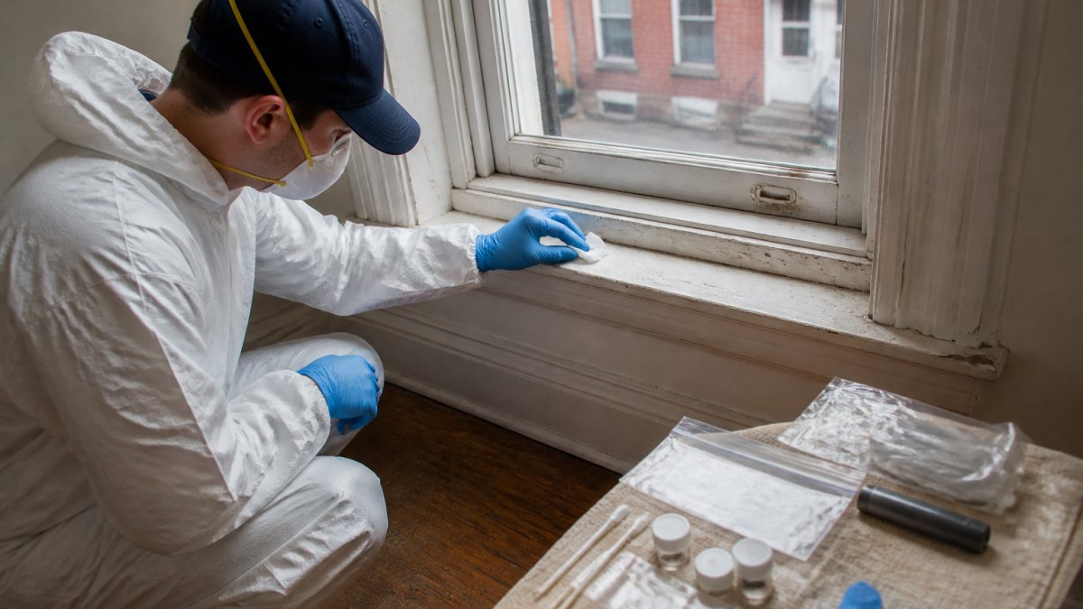 A certified lead inspector in gloves and protective gear using a wipe to sample a windowsill in an older Philadelphia rowhouse apartment, with testing supplies laid out nearby
