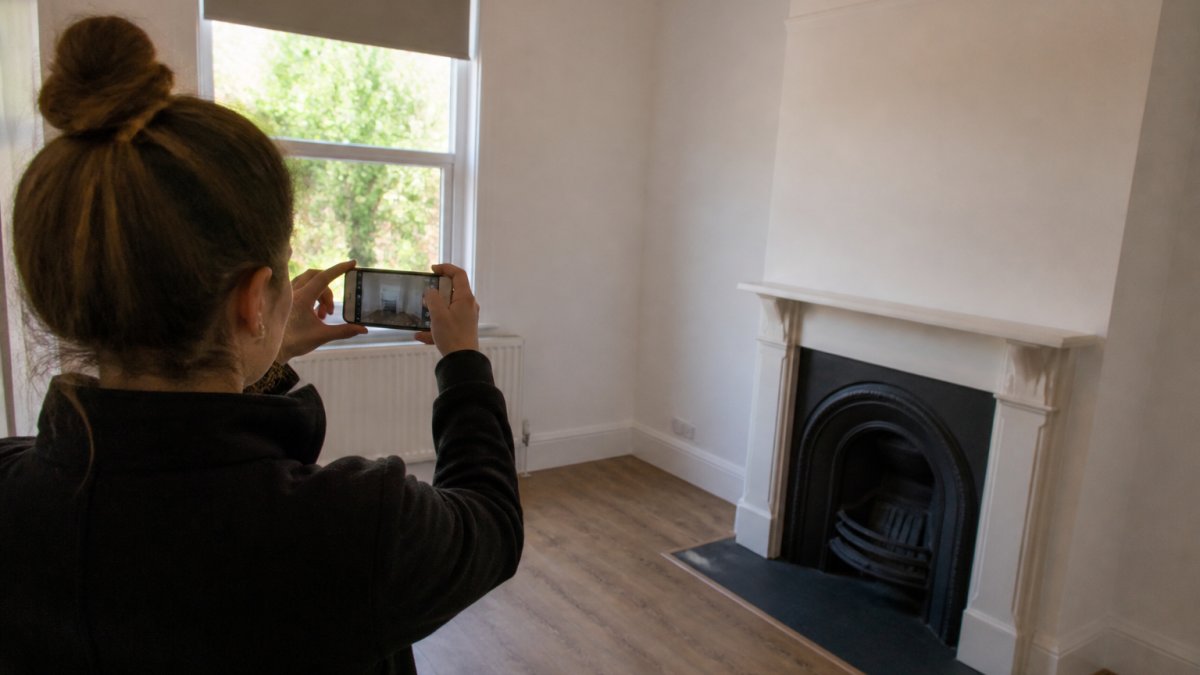 Tenant photographing room condition with smartphone, capturing walls, flooring, and fixtures during move-out inspection