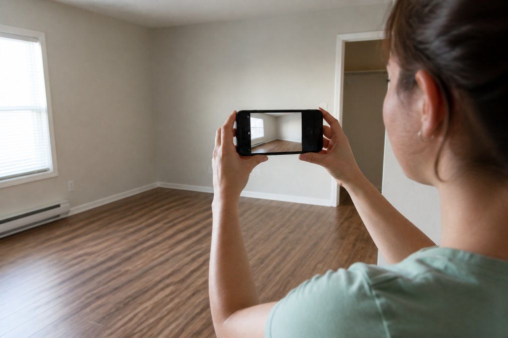 Tenant using a smartphone to photograph a clean apartment room to document its condition for a security deposit.