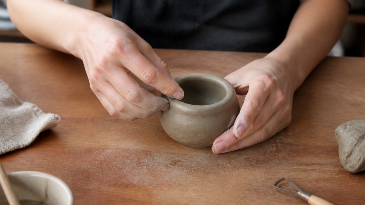 Step-by-step diagram showing the pinch pot technique for hand building pottery on a wooden work table.