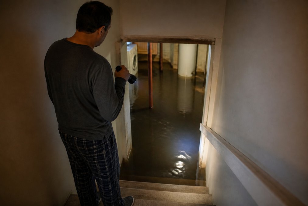 Homeowner in pajamas holding a flashlight while discovering a 2am flood in their dark basement.