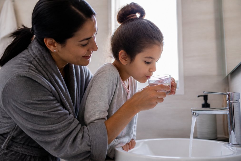 A parent gently helping a child rinse their mouth with warm water at a bathroom sink, soft natural light, both calm and focused