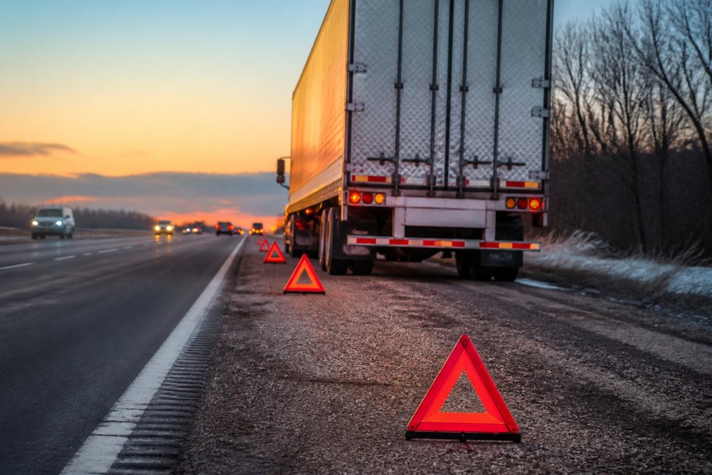 Semi-truck parked on a highway shoulder with hazard lights and warning triangles displayed during truck breakdowns