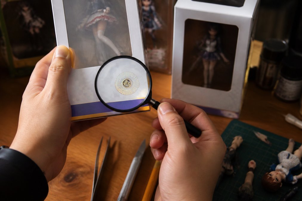 Hands examining a holographic sticker on a box to verify authentic anime figures on a collector's desk.