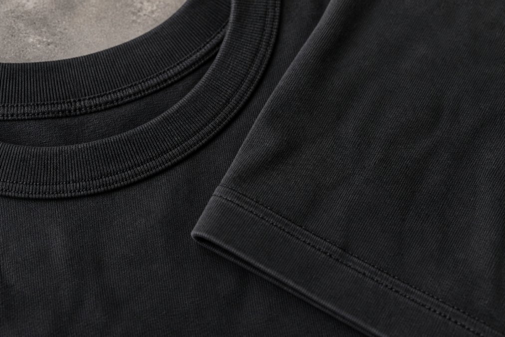 Detailed close-up of double-needle stitching on heavyweight tee's neckline and sleeve hem showing tight, even, parallel stitches with consistent spacing