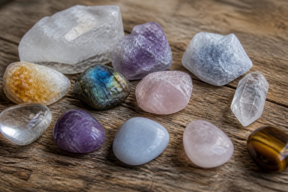 Close-up of several raw and tumbled natural crystals on a wooden surface, showing visible inclusions, natural fractures, and varied translucency under soft natural light