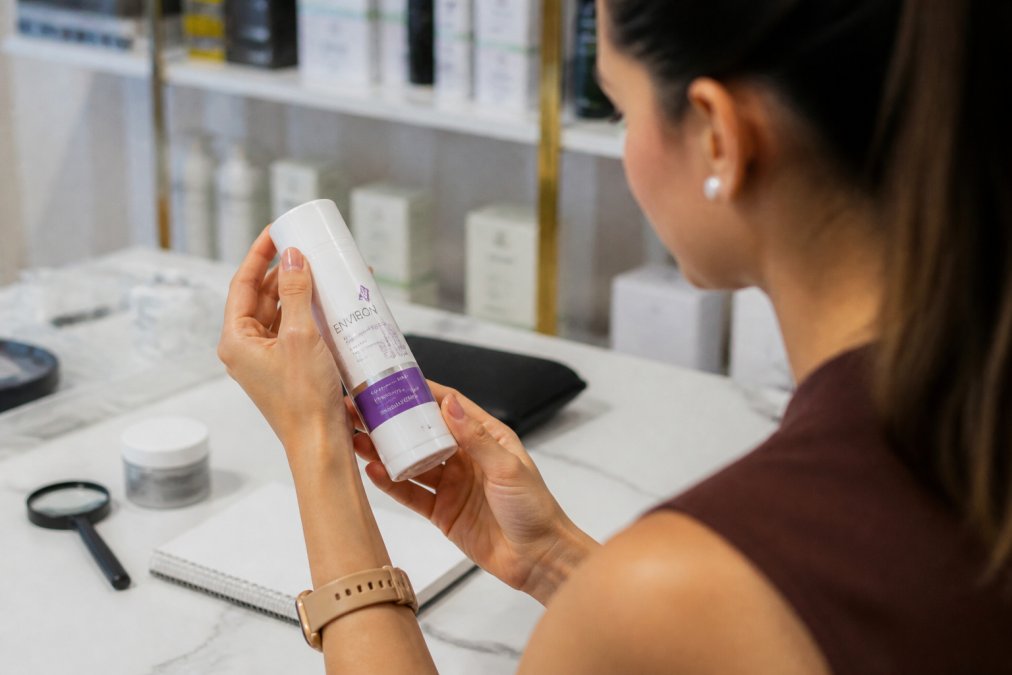 Close-up of hands holding a medical-grade skincare bottle, examining the label, batch code, and tamper-evident seal under natural light in a clinical setting