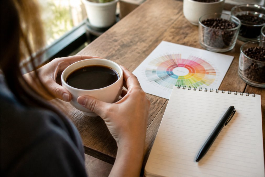 Infographic illustrating the process of identifying coffee tasting notes using a flavor wheel and notebook.
