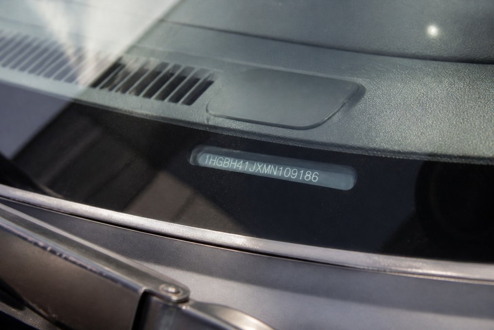 Close-up of a vehicle's dashboard showing the VIN plate clearly visible through the windscreen, with sunlight highlighting the identification number