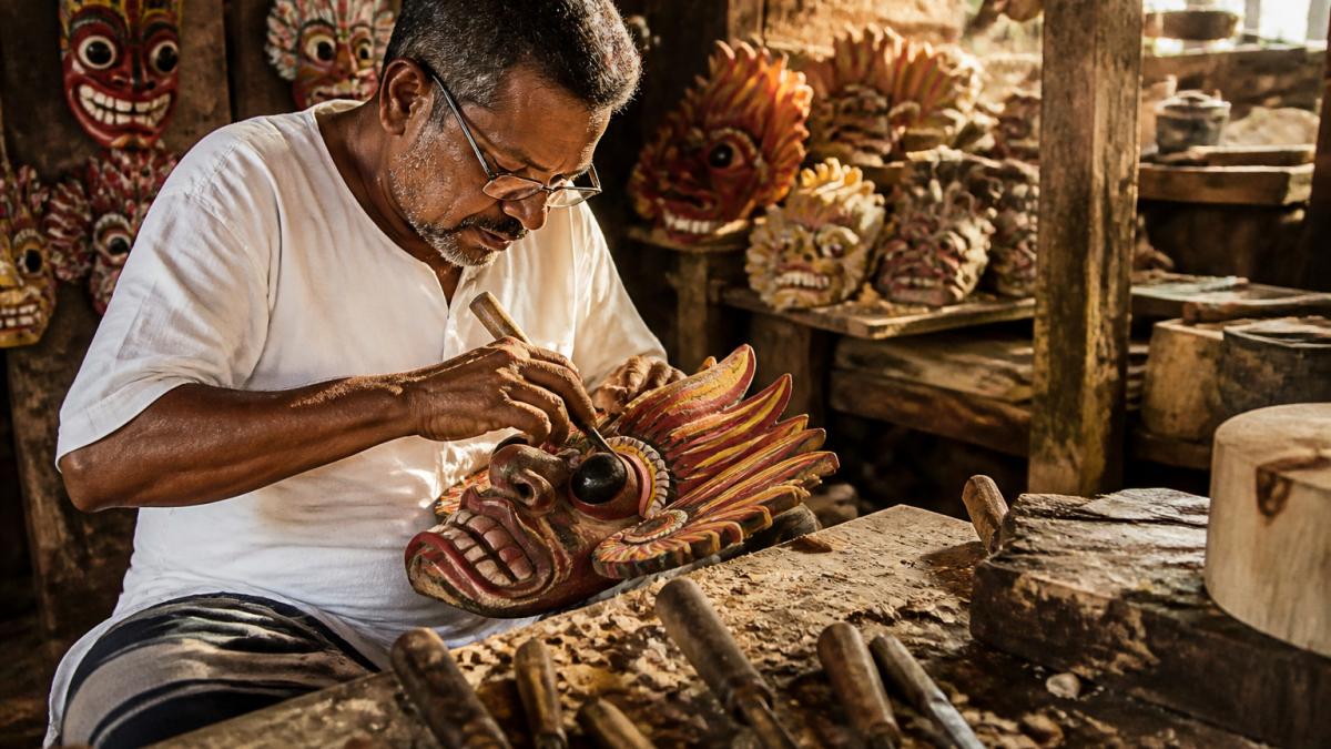 Sri Lankan artisan carving a traditional wooden ritual mask at a workbench in a village workshop