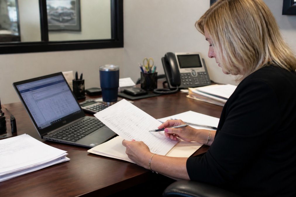 Office manager using a pen to review a DMS invoice for dealership billing errors at a desk