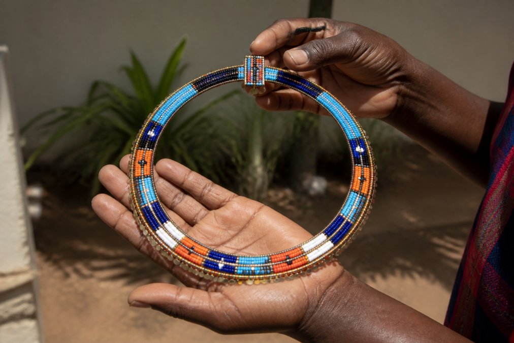 Close-up of hands holding a piece of handcrafted jewelry with intricate beadwork and traditional African design details visible, showing the meticulous craftsmanship and quality of authentic ethical pieces against natural sunlight