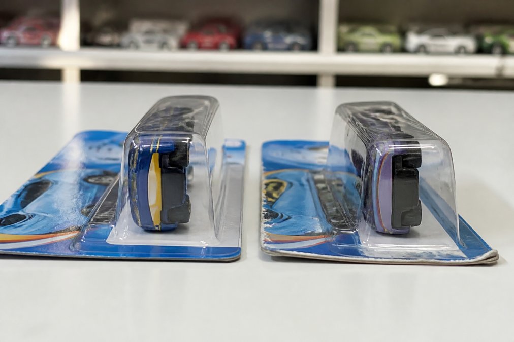 Close-up of two Hot Wheels blister cards placed side by side on a flat white surface, one with clean sealed edges and uniform card stock, the other with visible glue residue and slightly warped card edges, photographed under even studio lighting to show the contrast
