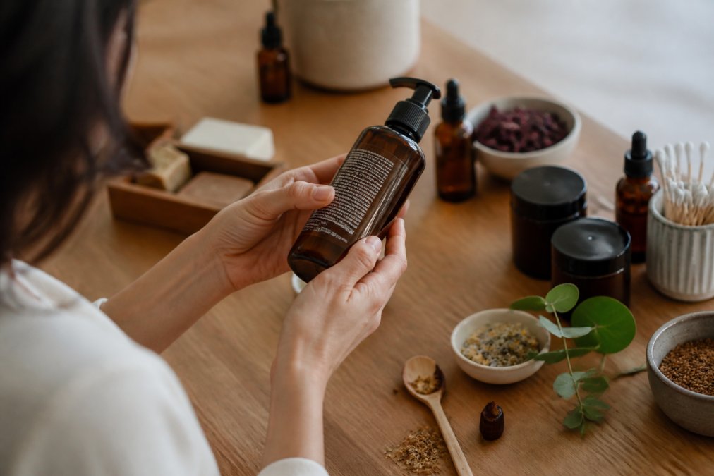 Close-up of a person's hands holding a skincare bottle, turning it to read the ingredient list on the back label in natural daylight