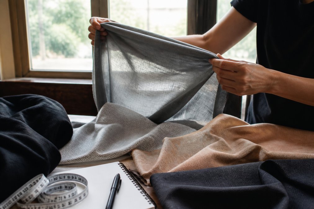 Close-up of hands examining fabric texture, holding a garment up to natural light to check transparency and weave structure, fingers testing the weight and drape of material across different sections