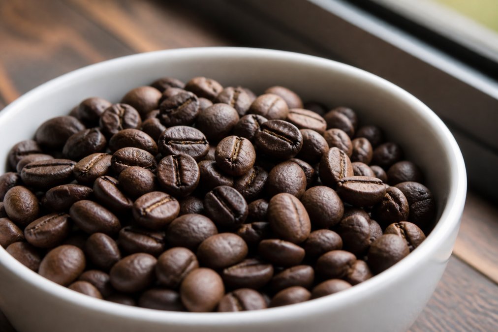 Close-up of coffee beans in a white ceramic bowl showing color uniformity, bean size variation, and surface texture details with natural window lighting