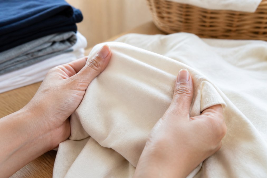 Hands holding and feeling a cotton t-shirt fabric, examining the texture and weight with fingers, natural indoor lighting