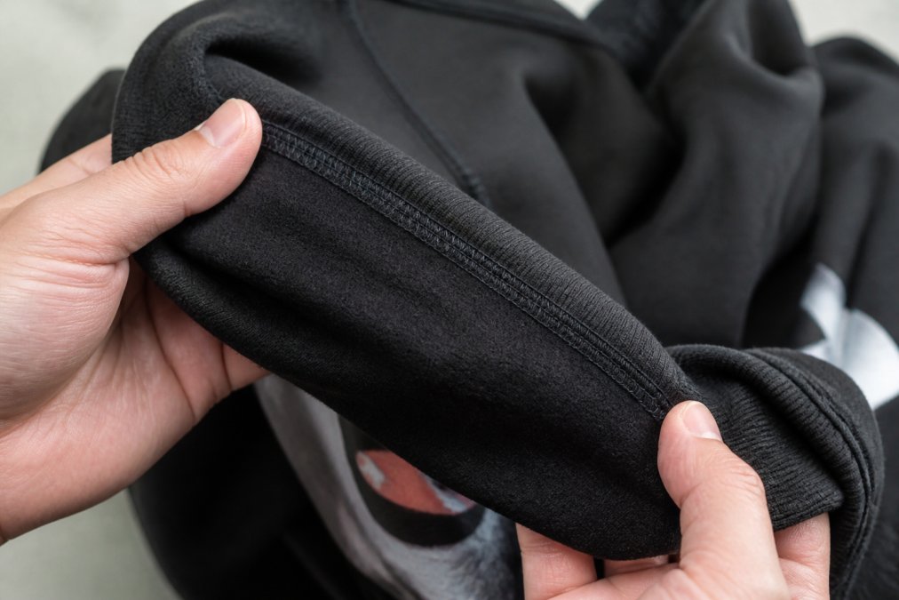 Diagram showing how to identify high quality graphic hoodies by examining double-stitched seams and ribbed cuffs.