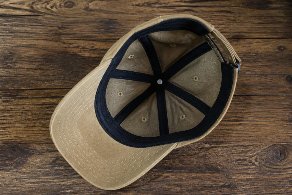 Close-up overhead view of a high-quality baseball cap laid flat on a wooden surface, showing the crown, pre-curved bill, structured visor, interior sweatband with visible stitching, and ventilation eyelets with clear detail of each construction element