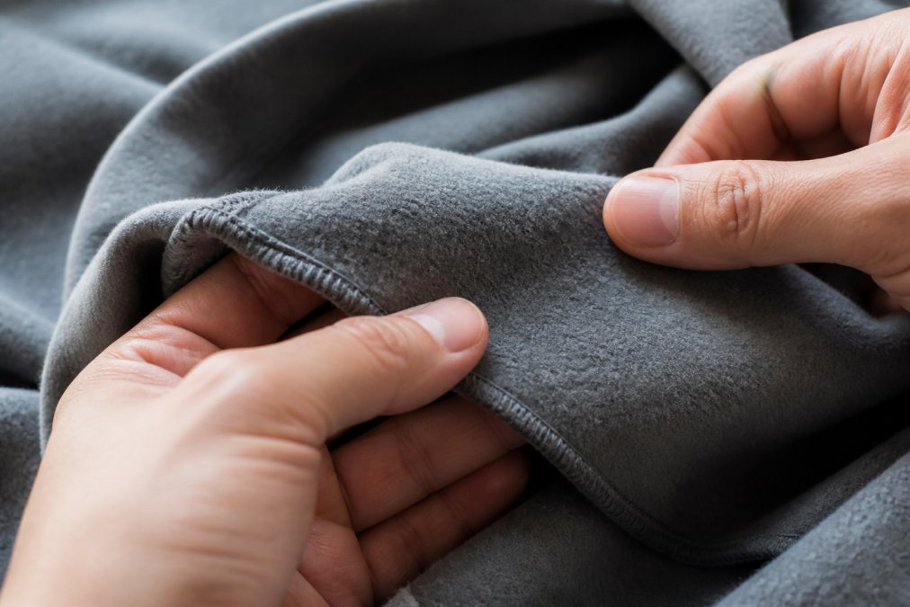 Close-up of hands running fingers across high-quality hoodie fleece interior, demonstrating tactile inspection with focus on softness and texture consistency