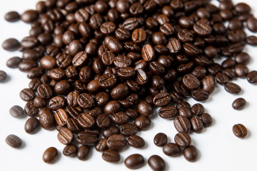 Close-up of freshly roasted specialty coffee beans spread on a white surface showing uniform dark brown color, consistent bean shape and size, and glossy surface with visible oil sheen