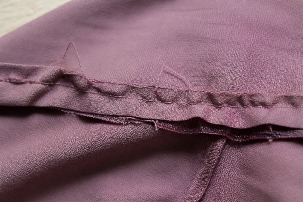 Detailed close-up of a poorly constructed seam showing visible puckering, loose threads, uneven stitch spacing, and frayed raw edges under bright lighting