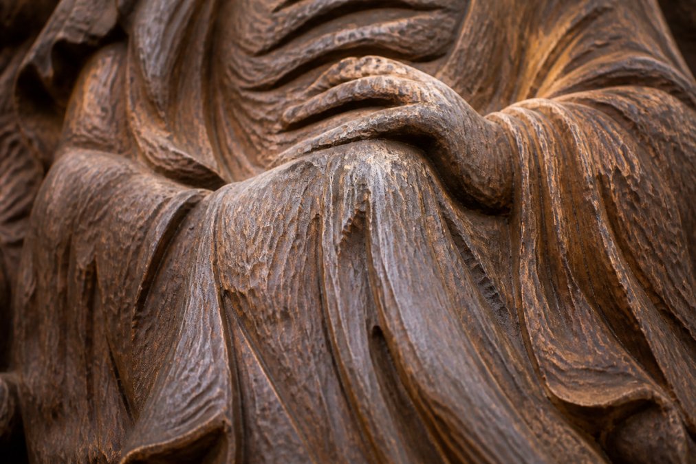 Close-up of hand-carved wood surface showing natural chisel marks, varied tool strokes creating organic texture patterns, and visible wood grain with uneven but intentional surface finish in natural lighting
