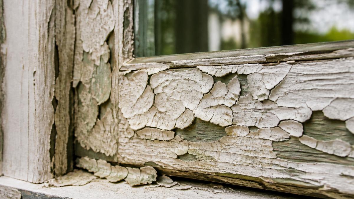 Close-up of peeling and chipping paint on a wooden window frame showing layers of paint deterioration and alligatoring patterns in an older home