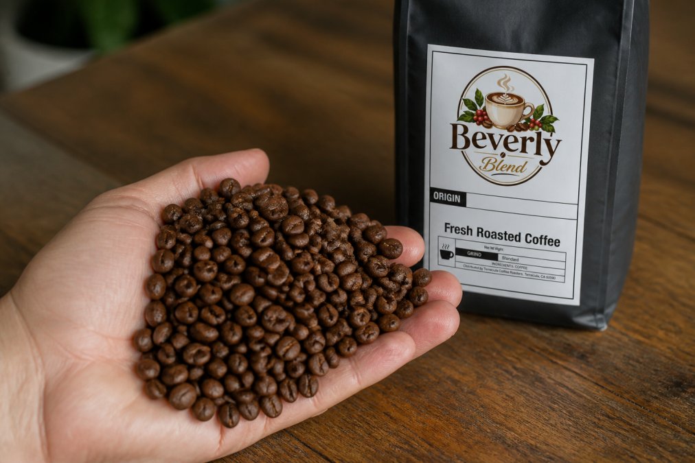 Close-up of freshly roasted coffee beans in a hand showing glossy surface and rich brown color, with a roast date label visible on a bag in the background