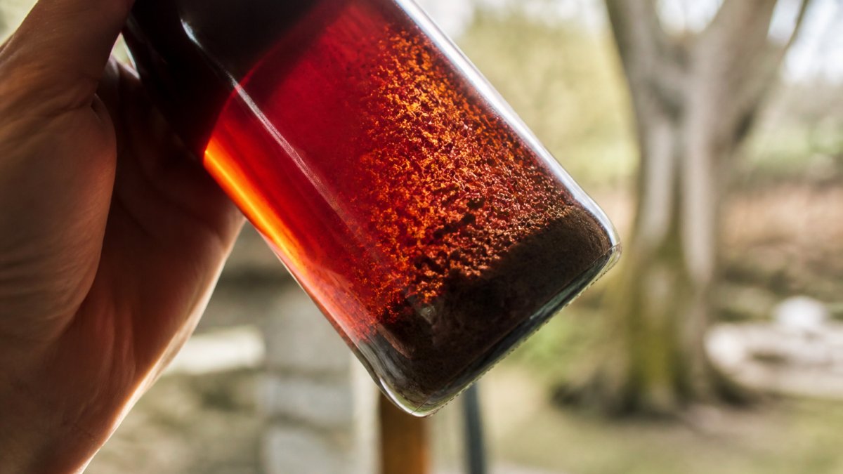 Diagram highlighting sediment particles and tartrate crystals inside an aged wine bottle held against sunlight.