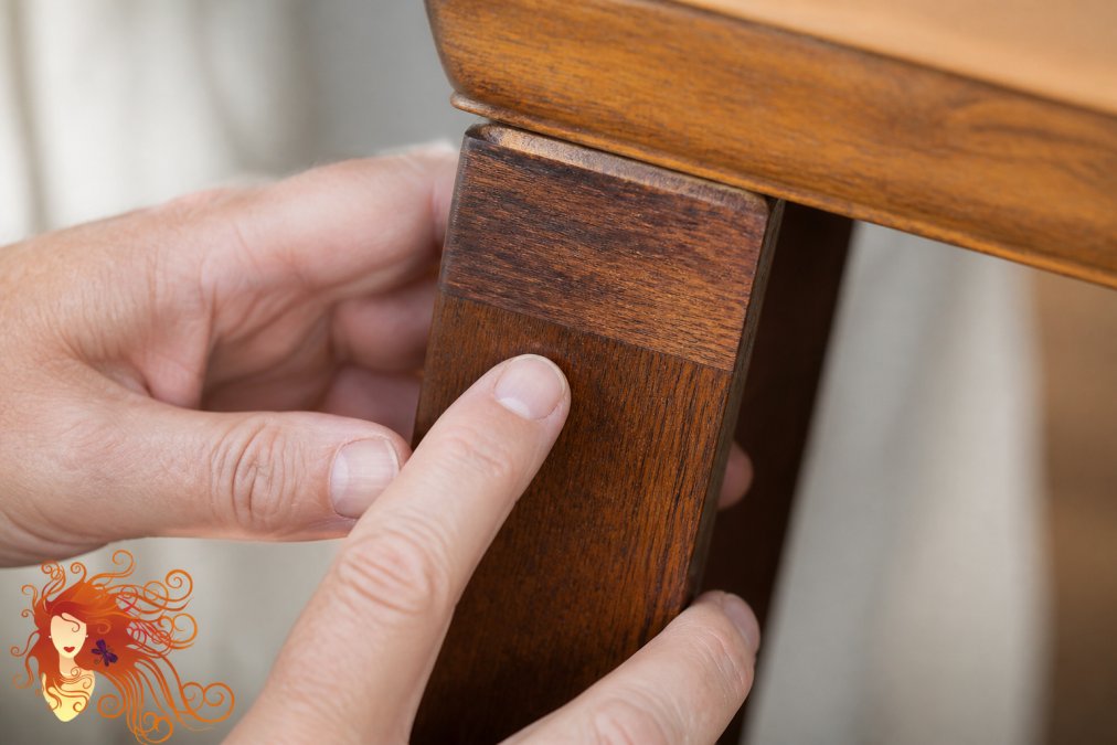 Close-up of hands examining the edge grain and surface grain of a wooden table leg in natural daylight, showing the wood's natural texture and grain pattern flowing along the edge